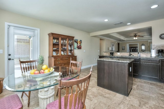 kitchen featuring dark brown cabinetry, sink, a center island, ceiling fan, and light stone countertops