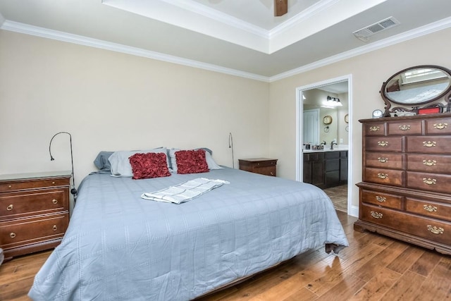 bedroom with crown molding, hardwood / wood-style floors, ensuite bathroom, and a tray ceiling