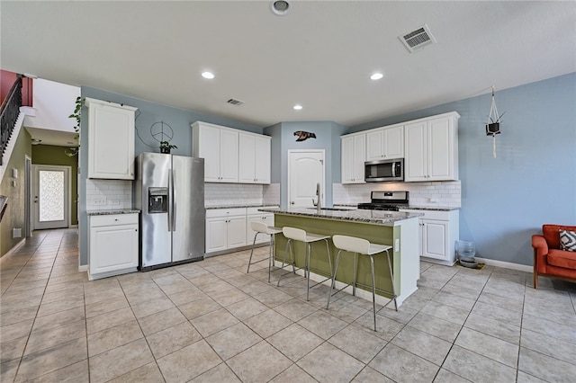 kitchen featuring light stone countertops, stainless steel appliances, white cabinets, and a center island with sink