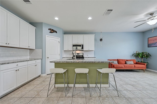 kitchen with a breakfast bar, light stone counters, white cabinetry, appliances with stainless steel finishes, and a kitchen island with sink