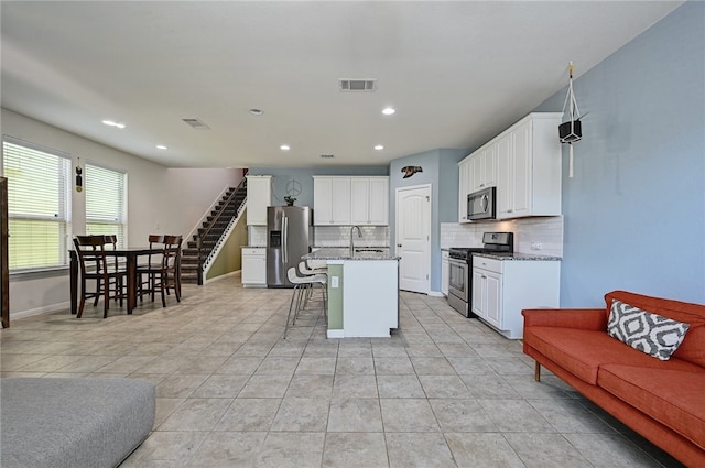kitchen featuring sink, appliances with stainless steel finishes, a kitchen island with sink, a kitchen breakfast bar, and light stone counters