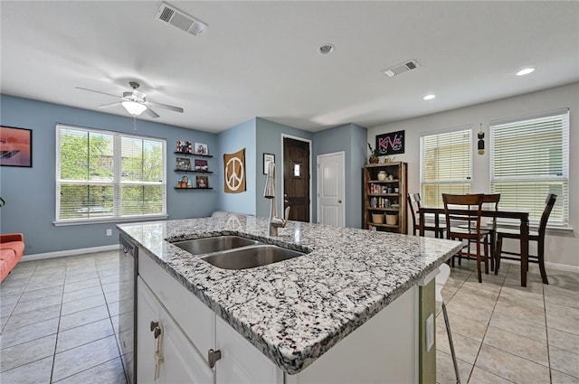 kitchen with light tile patterned floors, a breakfast bar area, white cabinetry, a kitchen island with sink, and light stone countertops