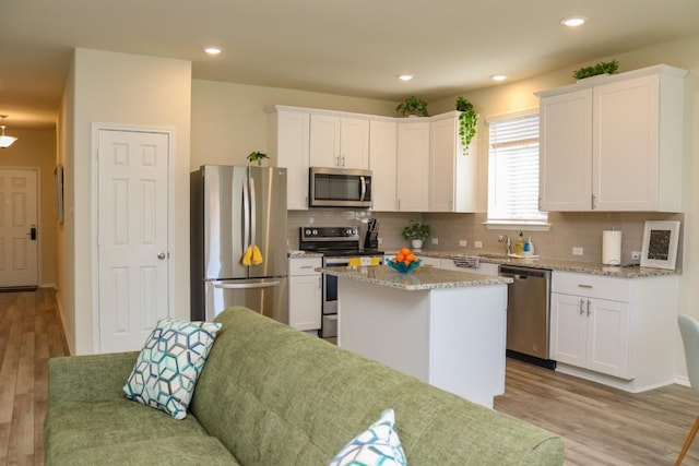 kitchen with stainless steel appliances, a center island, light stone counters, white cabinets, and light wood-type flooring