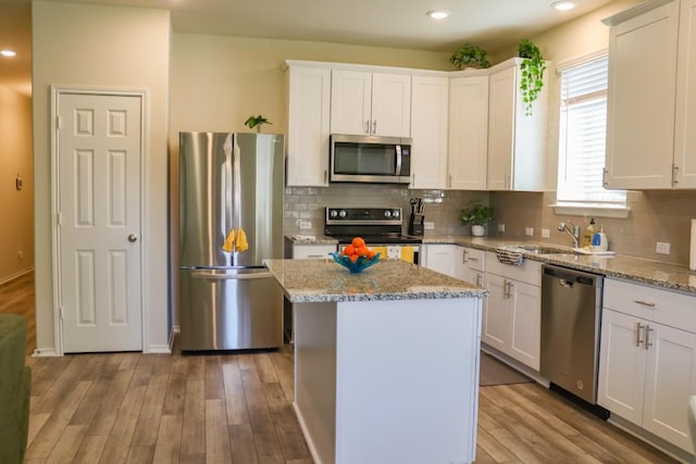 kitchen featuring light hardwood / wood-style flooring, stainless steel appliances, a center island, light stone counters, and white cabinets