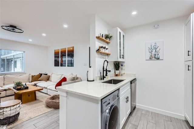 kitchen with white cabinetry, washer / dryer, sink, light stone counters, and light hardwood / wood-style flooring