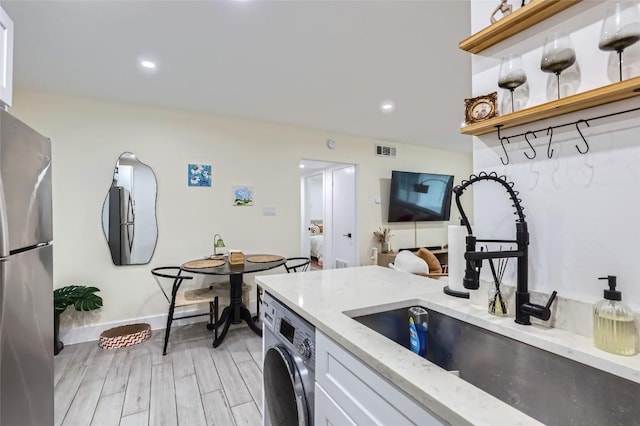 1200 E 52nd St Unit 108, Austin, TX 78723 - kitchen featuring freestanding refrigerator, washer / dryer, light stone countertops, open shelves, and light wood-type flooring