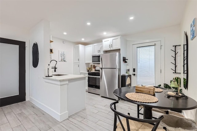 kitchen featuring stainless steel appliances, kitchen peninsula, sink, and white cabinets