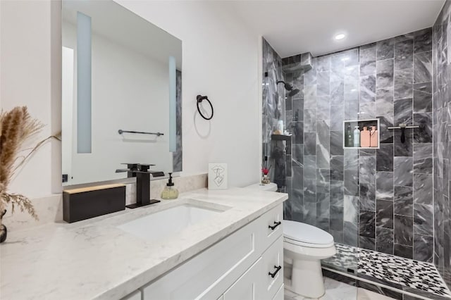 bathroom with a tile shower, vanity, and toilet