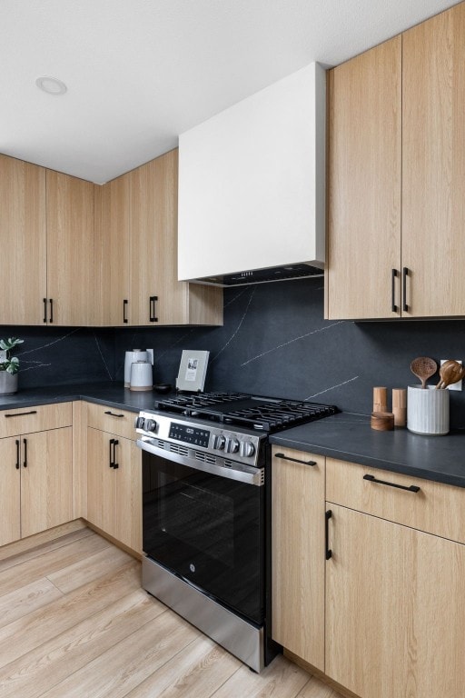 kitchen featuring stainless steel range with gas stovetop, decorative backsplash, light brown cabinets, and light hardwood / wood-style floors