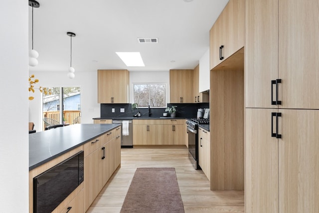 kitchen featuring sink, dishwasher, light brown cabinetry, gas range, and decorative light fixtures