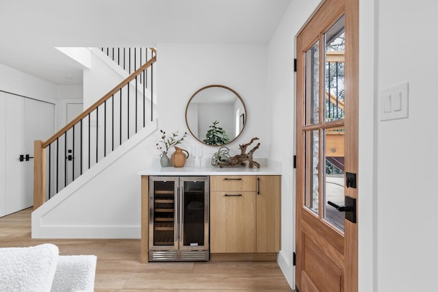 bar with light brown cabinets, beverage cooler, and light wood-type flooring