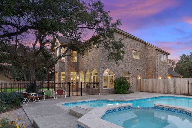 pool at dusk featuring an in ground hot tub and a patio