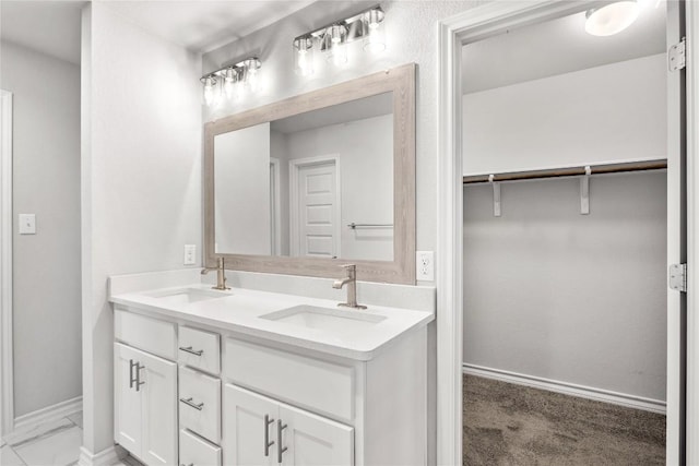 bathroom featuring double vanity, a sink, a walk in closet, and baseboards