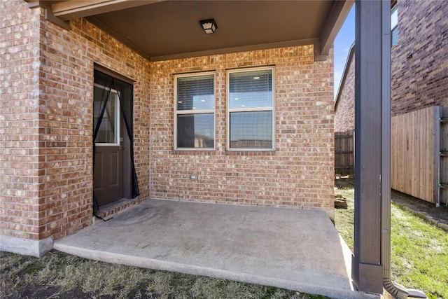 property entrance featuring a patio area, brick siding, and fence