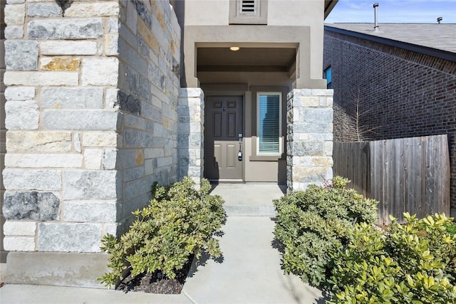 view of exterior entry featuring stone siding, fence, and stucco siding