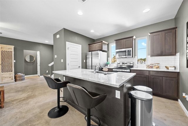 kitchen with sink, appliances with stainless steel finishes, backsplash, a center island with sink, and a kitchen bar