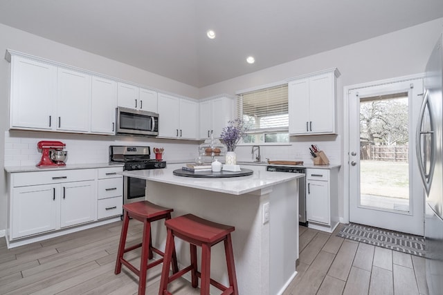 kitchen featuring a breakfast bar, white cabinetry, stainless steel appliances, a center island, and light wood-type flooring