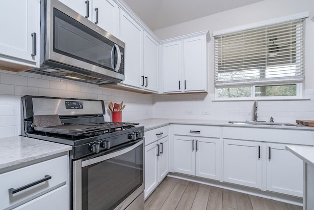 kitchen featuring sink, stainless steel appliances, tasteful backsplash, light stone countertops, and white cabinets