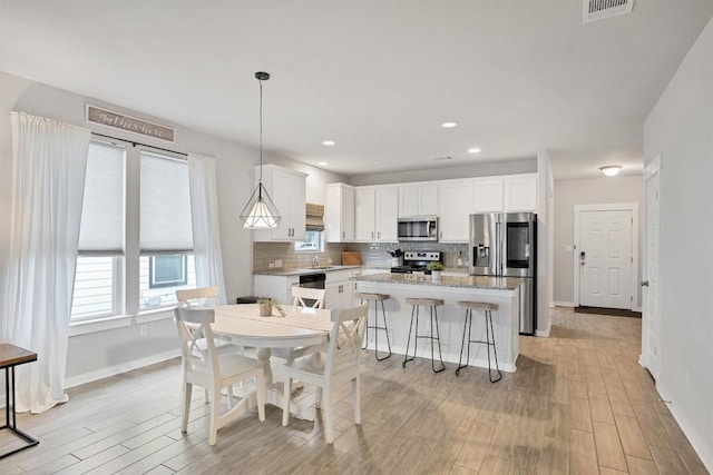 kitchen with a kitchen island, appliances with stainless steel finishes, pendant lighting, white cabinets, and backsplash