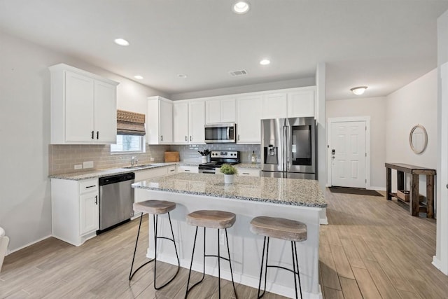 kitchen featuring a kitchen island, light stone countertops, appliances with stainless steel finishes, and white cabinets