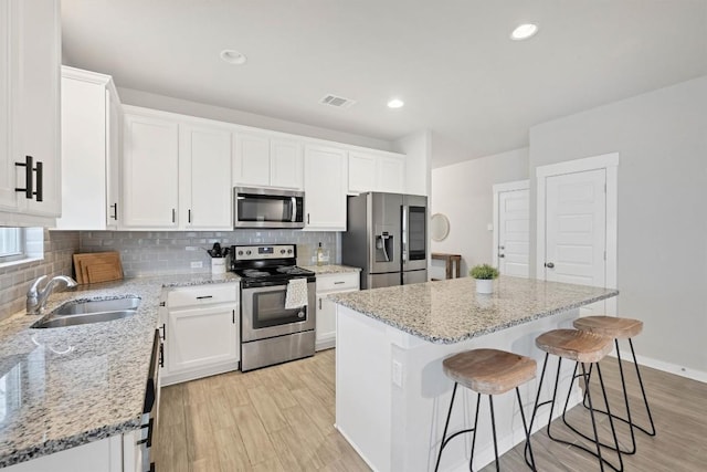 kitchen featuring sink, appliances with stainless steel finishes, a center island, light stone counters, and white cabinets