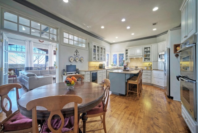 dining room featuring crown molding, light hardwood / wood-style floors, and beverage cooler