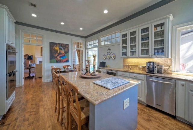 kitchen with a kitchen island, white cabinetry, light stone counters, stainless steel appliances, and crown molding