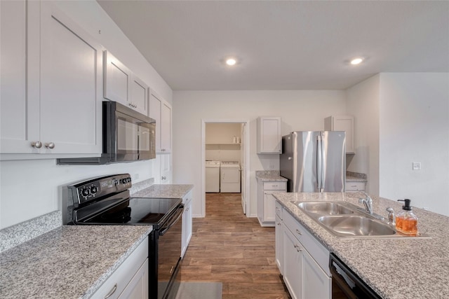 kitchen featuring sink, white cabinetry, light wood-type flooring, washing machine and dryer, and black appliances