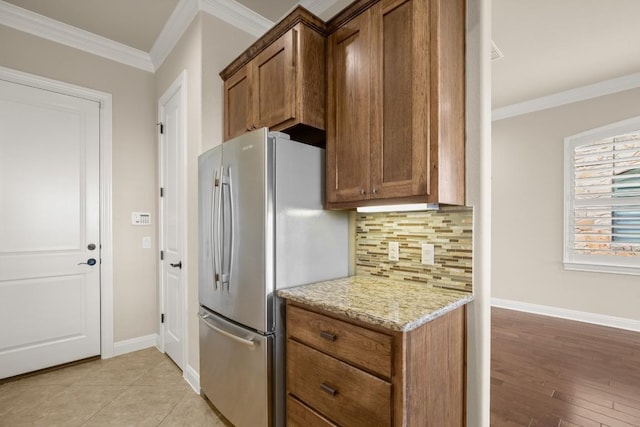 kitchen featuring stainless steel refrigerator, ornamental molding, light stone countertops, decorative backsplash, and light wood-type flooring