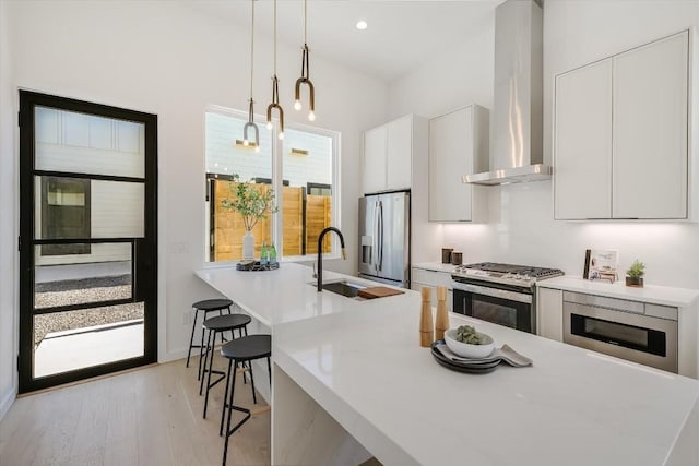 kitchen featuring sink, white cabinetry, decorative light fixtures, stainless steel appliances, and wall chimney range hood