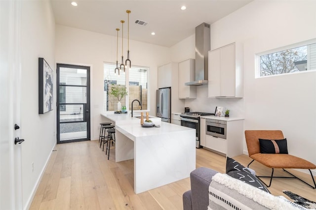 kitchen featuring light wood finished floors, wall chimney range hood, light countertops, appliances with stainless steel finishes, and white cabinets