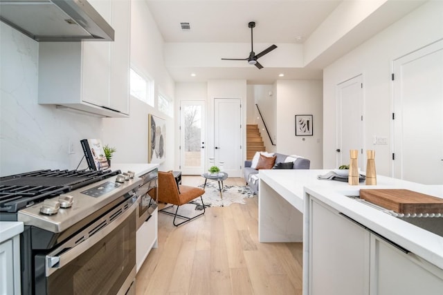 kitchen with light wood finished floors, visible vents, under cabinet range hood, stainless steel range with gas stovetop, and a ceiling fan