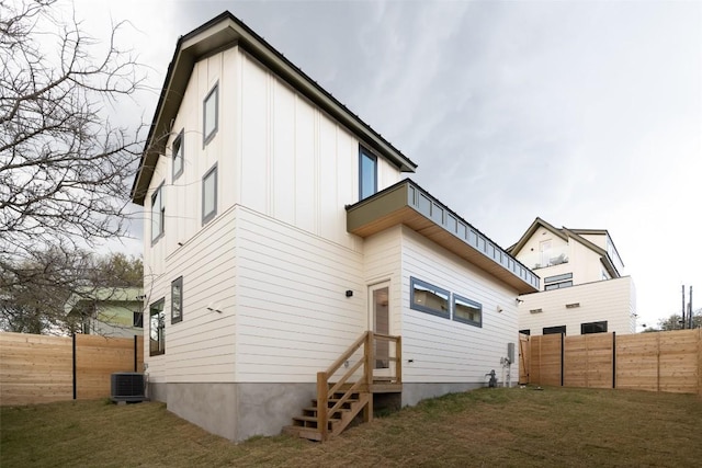 rear view of house featuring central AC unit, a yard, a fenced backyard, and board and batten siding