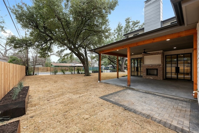 view of yard featuring an outdoor brick fireplace, a patio, and ceiling fan