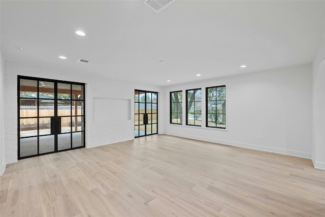 unfurnished room with light hardwood / wood-style flooring, french doors, and brick wall