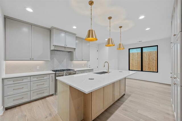 kitchen with pendant lighting, sink, a kitchen island with sink, light stone counters, and light hardwood / wood-style flooring