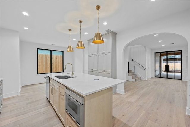 kitchen featuring sink, light hardwood / wood-style flooring, pendant lighting, stainless steel appliances, and a kitchen island with sink