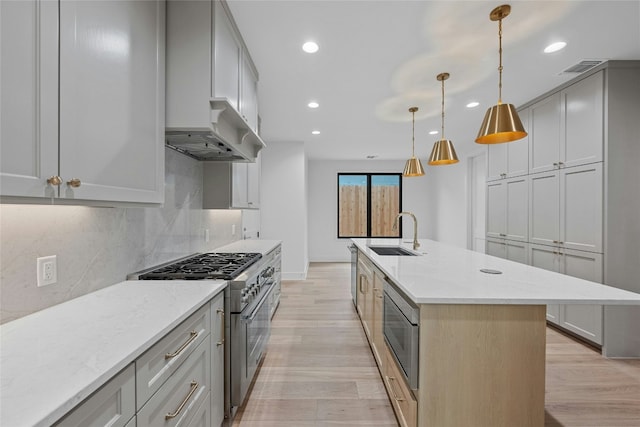 kitchen featuring sink, appliances with stainless steel finishes, decorative backsplash, a center island with sink, and decorative light fixtures