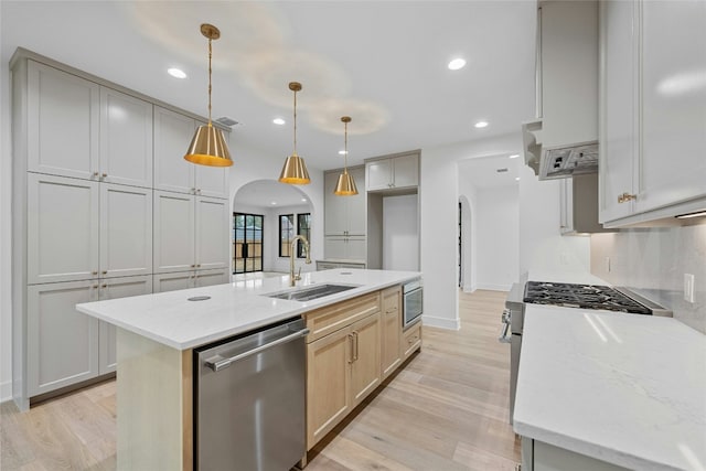 kitchen with appliances with stainless steel finishes, sink, hanging light fixtures, a kitchen island with sink, and light stone countertops