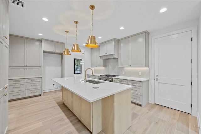 kitchen featuring an island with sink, sink, pendant lighting, and light hardwood / wood-style flooring