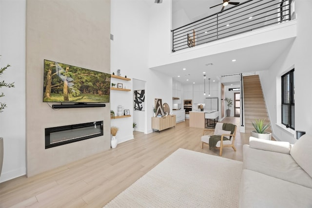 living room with a towering ceiling, ceiling fan, and light wood-type flooring