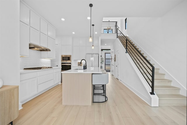 kitchen featuring sink, hanging light fixtures, light wood-type flooring, stainless steel appliances, and a kitchen island with sink