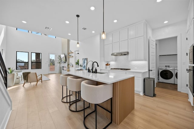 kitchen featuring visible vents, decorative backsplash, washer and clothes dryer, under cabinet range hood, and a sink