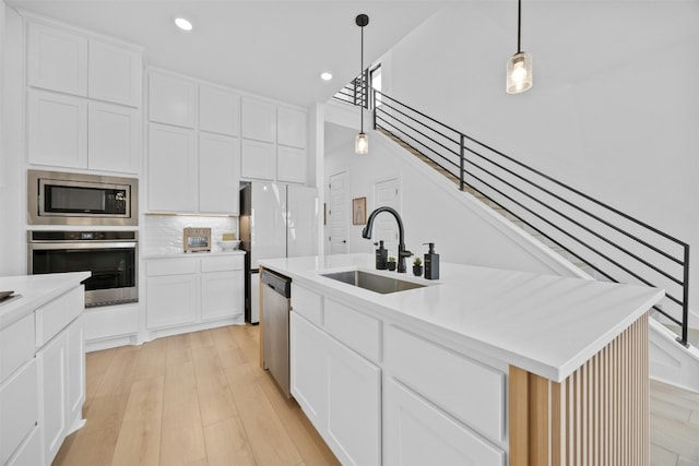 kitchen with sink, hanging light fixtures, stainless steel appliances, white cabinets, and a center island with sink