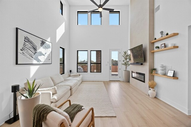 living area featuring wood finished floors, a glass covered fireplace, visible vents, and baseboards