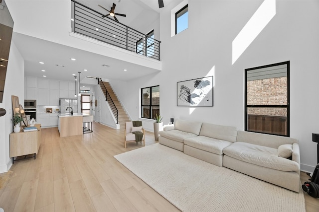 living room featuring a high ceiling, ceiling fan, sink, and light wood-type flooring