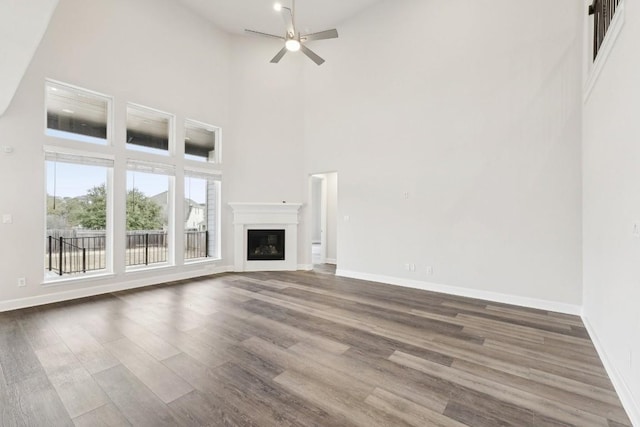 unfurnished living room featuring dark hardwood / wood-style floors, ceiling fan, and a towering ceiling