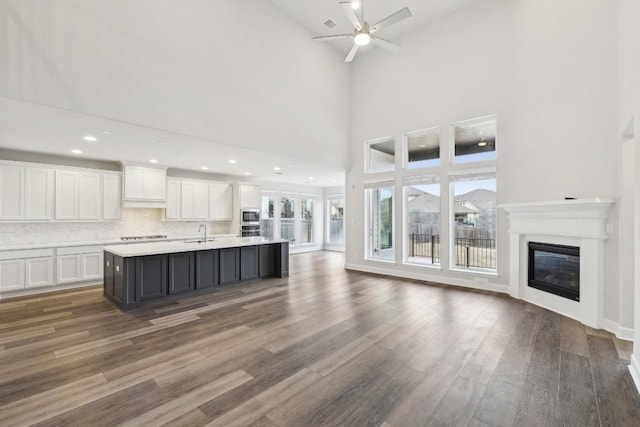 kitchen featuring a kitchen island with sink, white cabinetry, dark hardwood / wood-style floors, tasteful backsplash, and stainless steel microwave