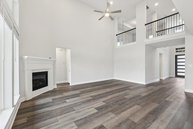 unfurnished living room featuring dark wood-type flooring, ceiling fan, and a high ceiling