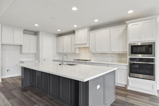 kitchen with appliances with stainless steel finishes, white cabinetry, sink, dark wood-type flooring, and a center island with sink